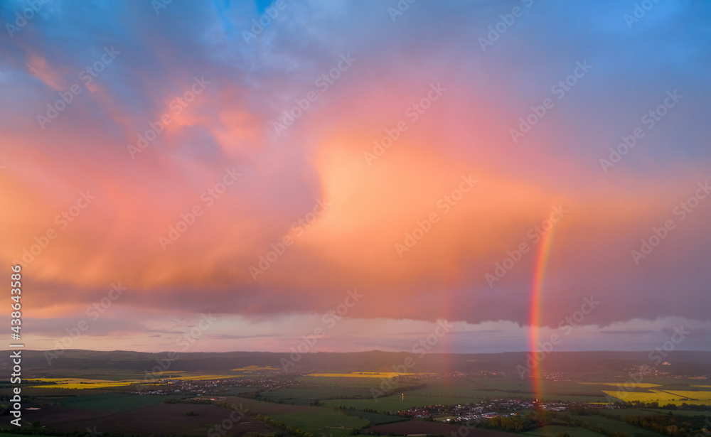 Evening, vibrant sky, pink violet blue clouds lit by setting sun. Huge rainbow over agriculture landscape. Aerial view, far horizon, ideal for sky replacement process.
