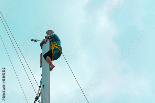 Sailor on top of sailing boat mast doing maintenance or radar system, mast harness human lifting system