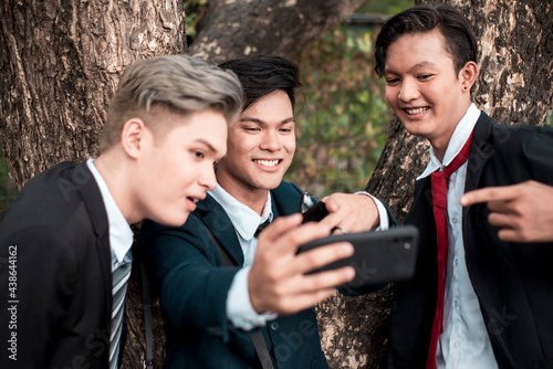 Three friends watch a funny viral video on social media playing on a cellphone. Bonding among young asian men outdoors photo