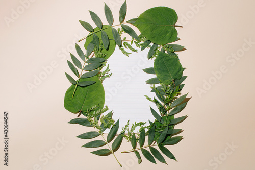 Creative layout made of leaves with white paper against pastel sand background. Minimal summer frame concept. photo