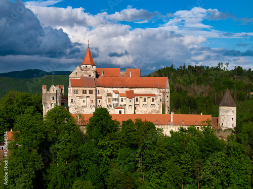 Ancient royal Moravian castle Pernstejn, standing on a hill covered green forest against partly cloudy blue sky. Aerial photography. Bohemian-Moravian Highlands, Czech landscape, travel point.
