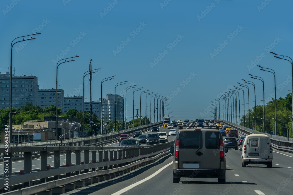 A toned image of a cityscape with sun flares. Car traffic on the road in summer in Moscow.