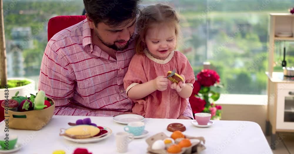 happy father and toddler baby daughter playing together with toy food at the rooftop patio, a home tea party happy father and toddler baby daughter playing together with toy food at the rooftop patio, a home tea party