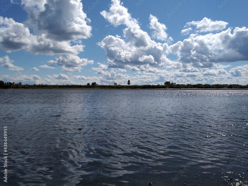 white clouds in the blue sky, the river bank, the horizon. summer day