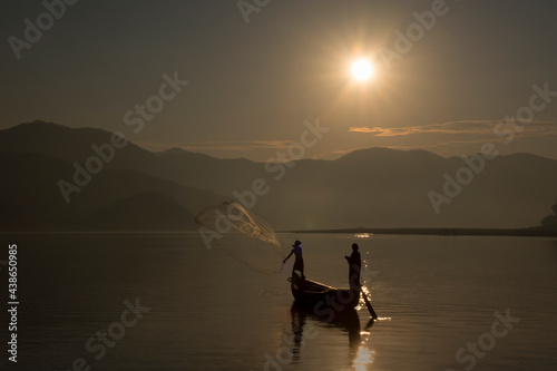 Fishermen throwing the fishing net in the river to catch the fish during sunrise