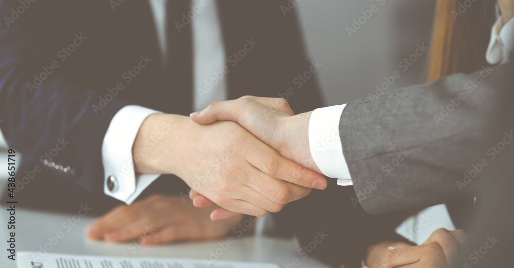 Unknown businessman shaking hands with his colleague or partner above the glass desk in modern office, close-up. Business people group at meeting Unknown businessman shaking hands with his colleague or partner above the glass desk in modern office, close-up. Business people group at meeting