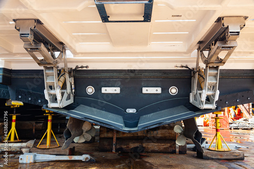 Aft with two propellers of the luxury motor yacht is dry docked on wooden blocks and supported by steel supports.