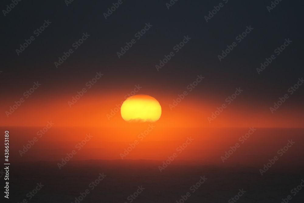Dark orange sunset over the Atlantic Ocean. Only the bottom part of the sun is visible in the sky.