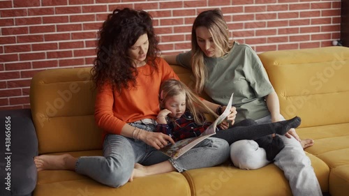 Young women read a book together to a small preschool girl on sofa photo