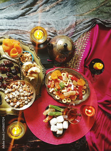 A table with Turkish tea with lale, oriental sweets, rahad delight, a mix of various nuts using copper dishes and bright fabrics.