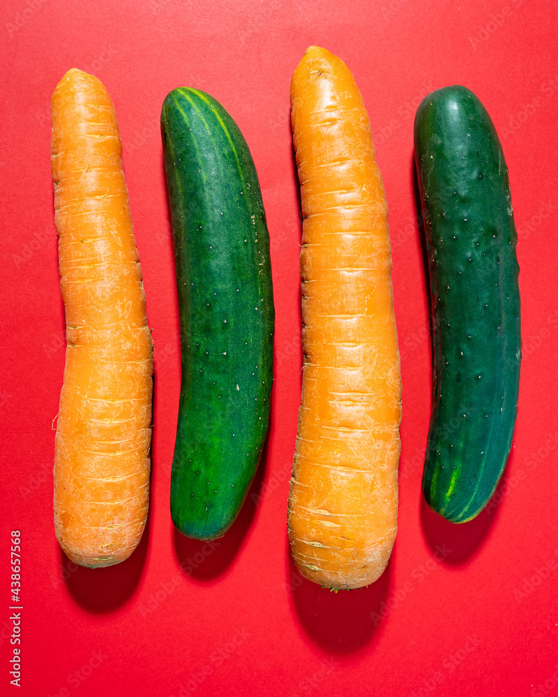 Raw cucumbers and carrots next to each other on red background Raw cucumbers and carrots next to each other on red background