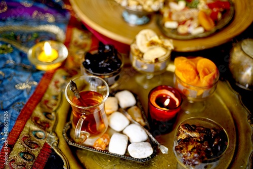 A table with Turkish tea with lale, oriental sweets, rahad delight, a mix of various nuts using copper dishes and bright fabrics. © natayurchuk