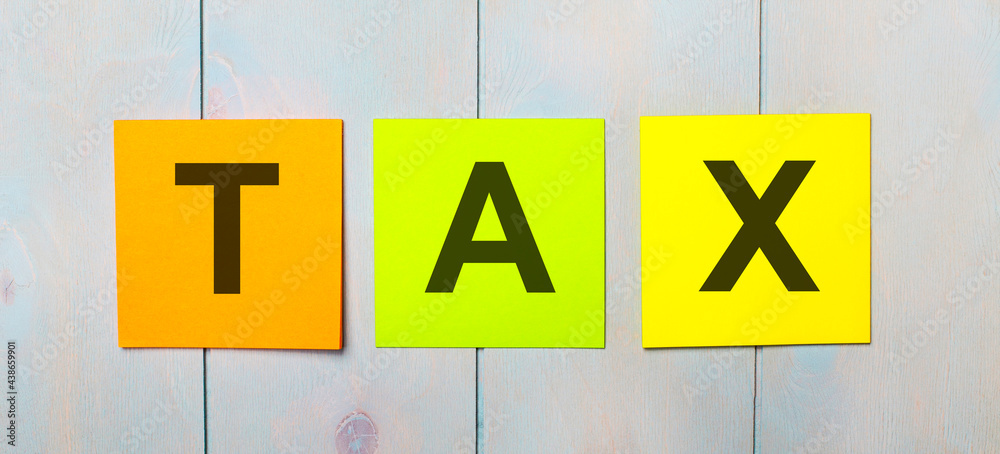 Three colored stickers with the text TAX on a light blue wooden background Three colored stickers with the text TAX on a light blue wooden background