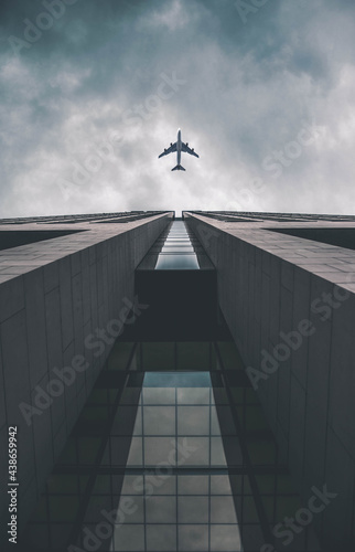 Low angle view of modern tall business building. Commercial jet plane flying over skyscraper. Against dramatic cloudy sky before storm.
