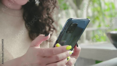 Young cheerful curly girl flips the phone and smiles sitting at the table in the restaurant