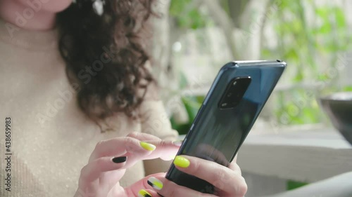 Young cheerful curly girl flips the phone and smiles sitting at the table in the restaurant