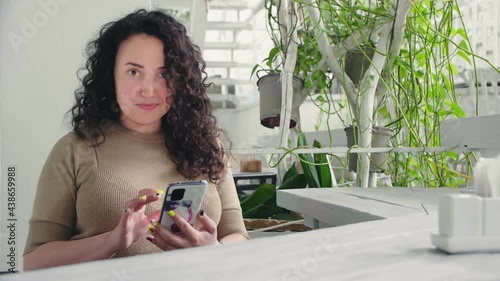 Young serious curly girl flips the phone sitting at the table in the restaurant