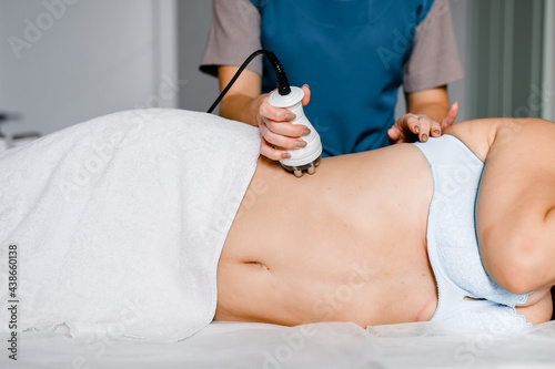 Skin and body care. Woman receives an electric massage against cellulite. Close-up of the apparatus massages belly and legs of woman.