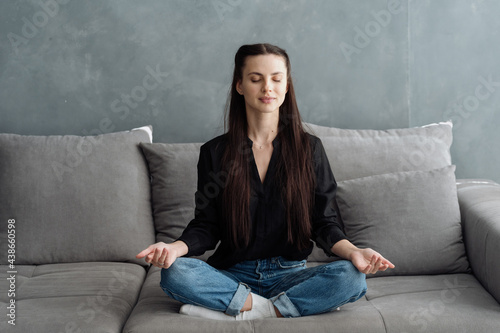 Young woman meditating, sitting on comfort couch