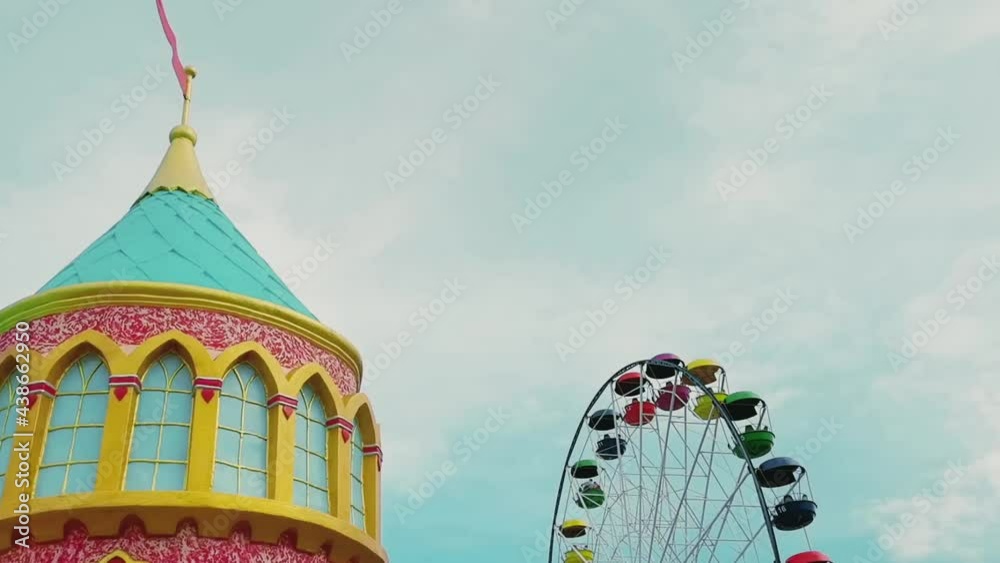 A rotating Ferris wheel in an amusement park against a blue sky.