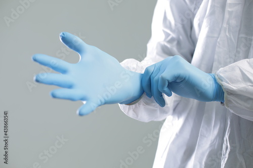 Doctor in a protective medical suit puts on blue rubber gloves