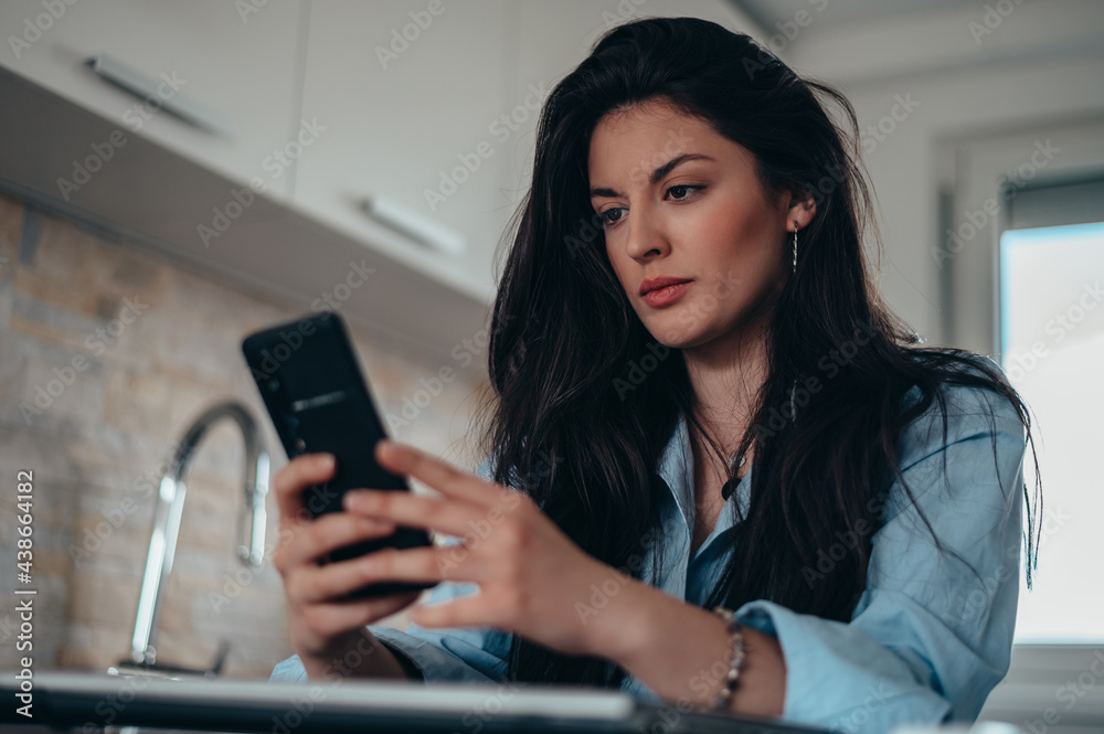 Businesswoman using her smartphone while spending morning in the kitchen