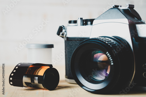 Old 35mm SLR film camera and a roll of film on wooden background. Flim photography concept. photo