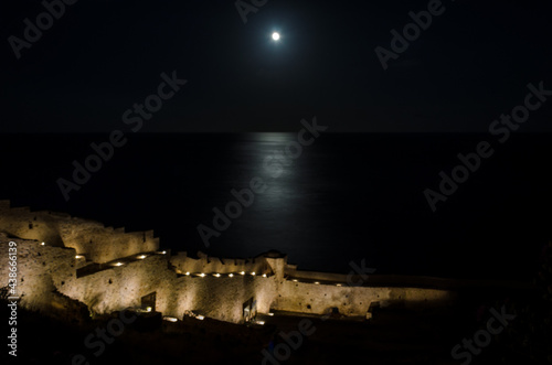 Beautiful Moonlight Reflection on Dark Medeterannean Sea Waters Surface Outside the Illuminated Monemvasia Island Medieval Castle Walls in Greece.
