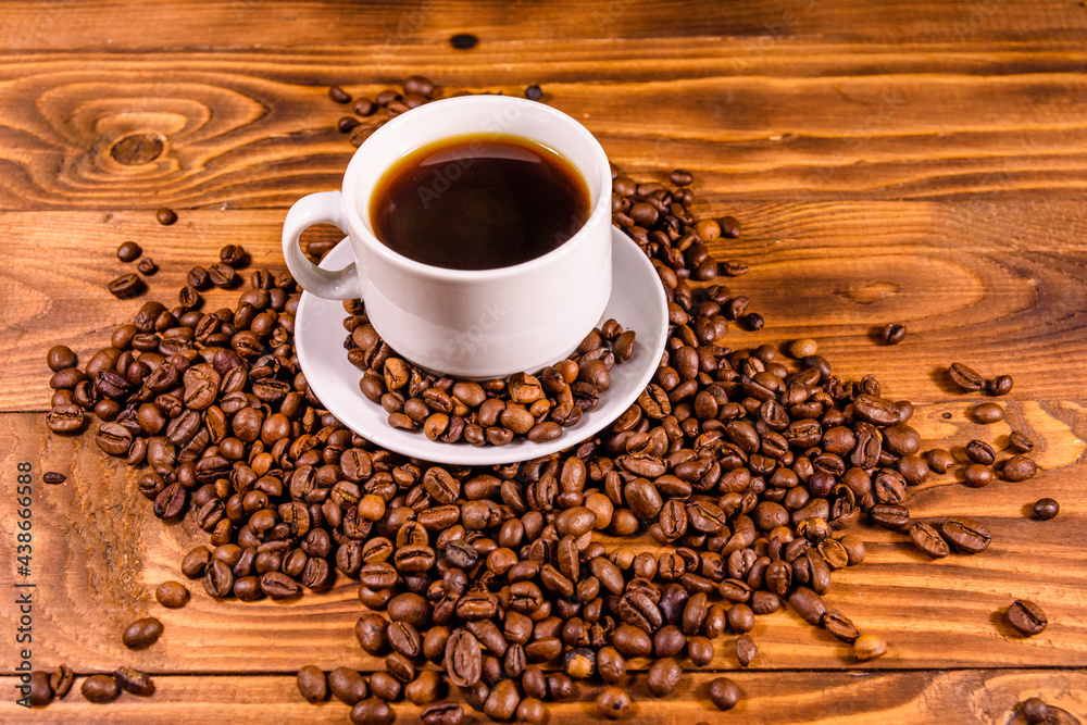 Obraz premium Cup of hot coffee and scattered coffee beans on wooden table