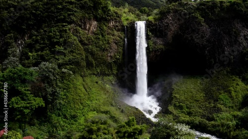 Aerial view, zooming in a a large waterfall until close to the water falling down and splashing 