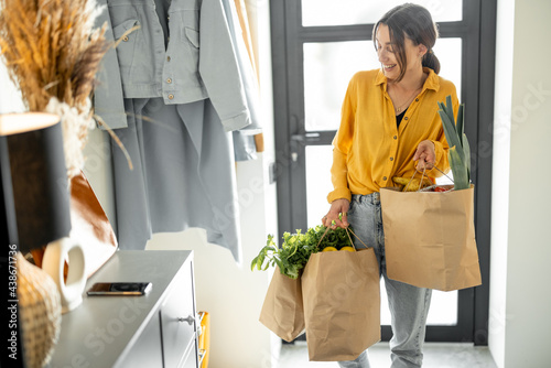 Woman comes home with bags full of fresh groceries, shopping healthy food in eco-packaging. Concept of buying food online and delivering it home