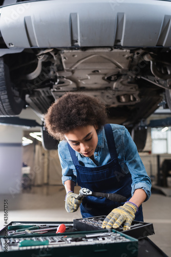 young african american mechanic standing beneath lifted car in garage