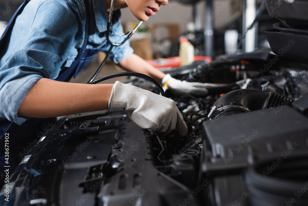 partial view of young african american mechanic in gloves and stethoscope working with car motor in garage partial view of young african american mechanic in gloves and stethoscope working with car motor in garage