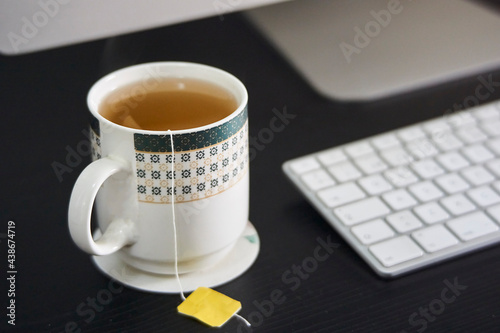 Close-up of a cup of hot tea on a desk with a computer