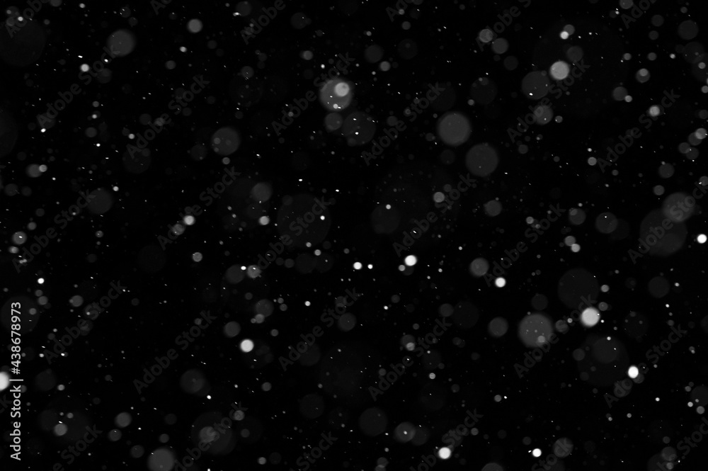 Bokeh of white snow on a black background. Falling snowflakes on night sky background, isolated for post production and overlay in graphic editor.