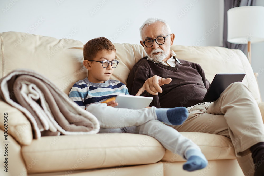 Senior man teaching his grandson watching something on touchpad while relaxing at home.