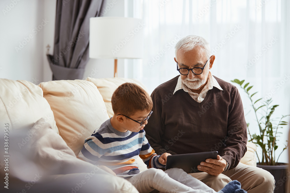 Small boy using digital tablet with his grandfather at home. Small boy using digital tablet with his grandfather at home.