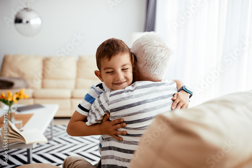 Happy little boy embracing his grandfather with eyes closed at home.