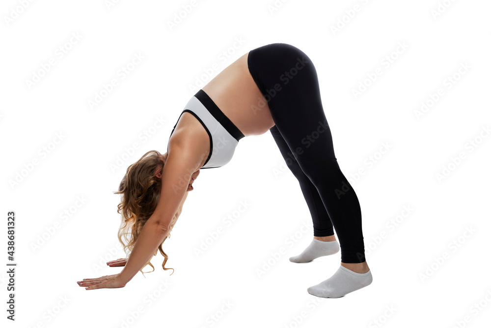 Young pregnant woman in sports uniform is doing exercises. Blonde in a downward facing dog pose. An active lifestyle and care for the health of the baby. Isolated on white background. Young pregnant woman in sports uniform is doing exercises. Blonde in a downward facing dog pose. An active lifestyle and care for the health of the baby. Isolated on white background.