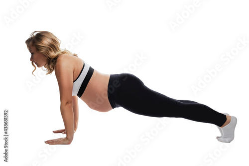 Young pregnant woman in sports uniform is doing exercises. The blonde is in the plank. An active lifestyle and care for the health of the baby. Isolated on white background.