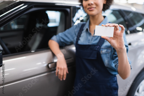partial view of young african american mechanic showing empty card and standing near car in garage