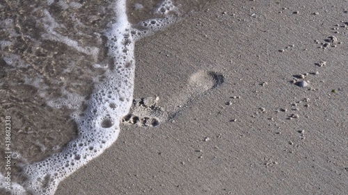 Fotografija Sea foam surf at clean white sand with footprint of barefoot legs