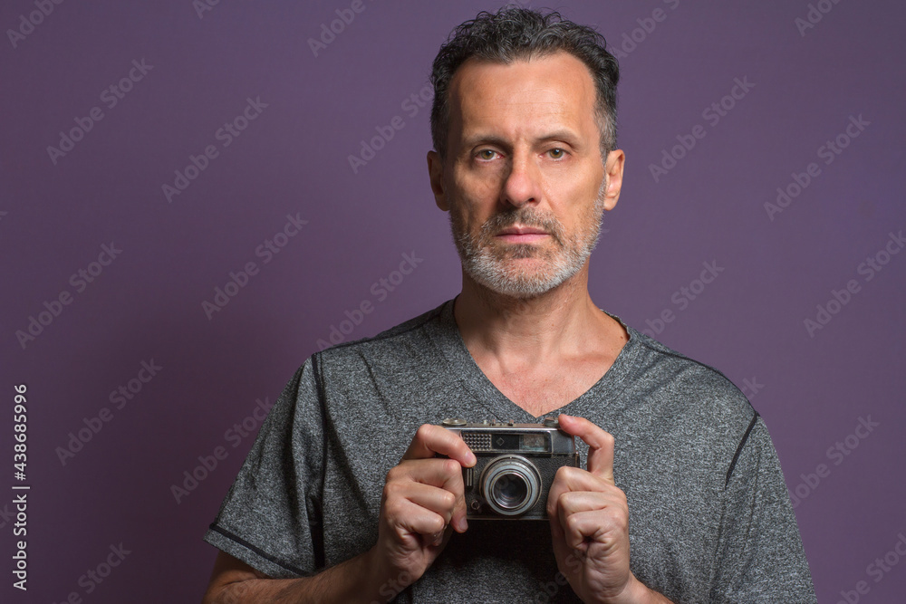 Portrait of a professional photographer isolated on a purple background holding a vintage camera in his hands. Portrait of a professional photographer isolated on a purple background holding a vintage camera in his hands.