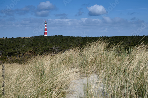 Classic  historic old red and white lighthouse with dunes and grass  sunny windy day and turbulent clouds on the Dutch island of Ameland  Hollum  April 2021