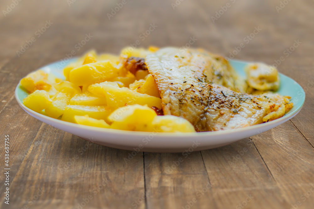 Fried fish in oil with herbs and spices with homemade fried potato. Simple, homemade food on wooden background. Fried fish in oil with herbs and spices with homemade fried potato. Simple, homemade food on wooden background.