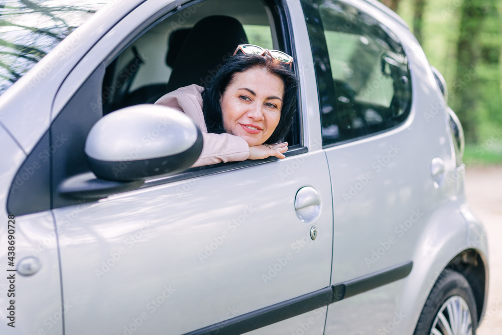 A beautiful woman of Caucasian appearance is sitting in her car, looking through the window