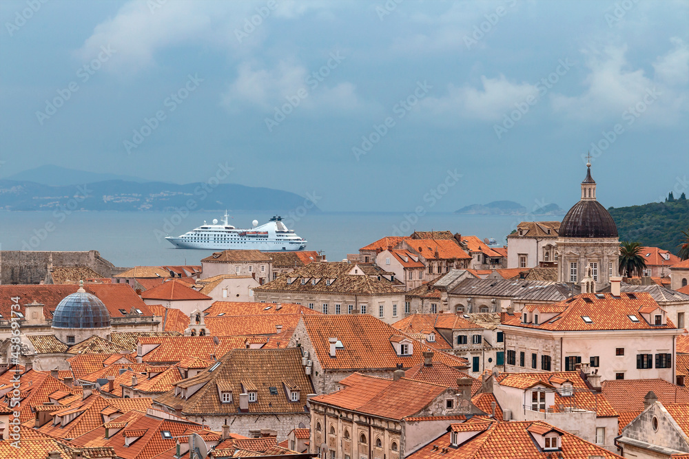 top view of the red tiled roofs of the ancient Croatian city of Dubrovnik and a white cruise ship on the sea
