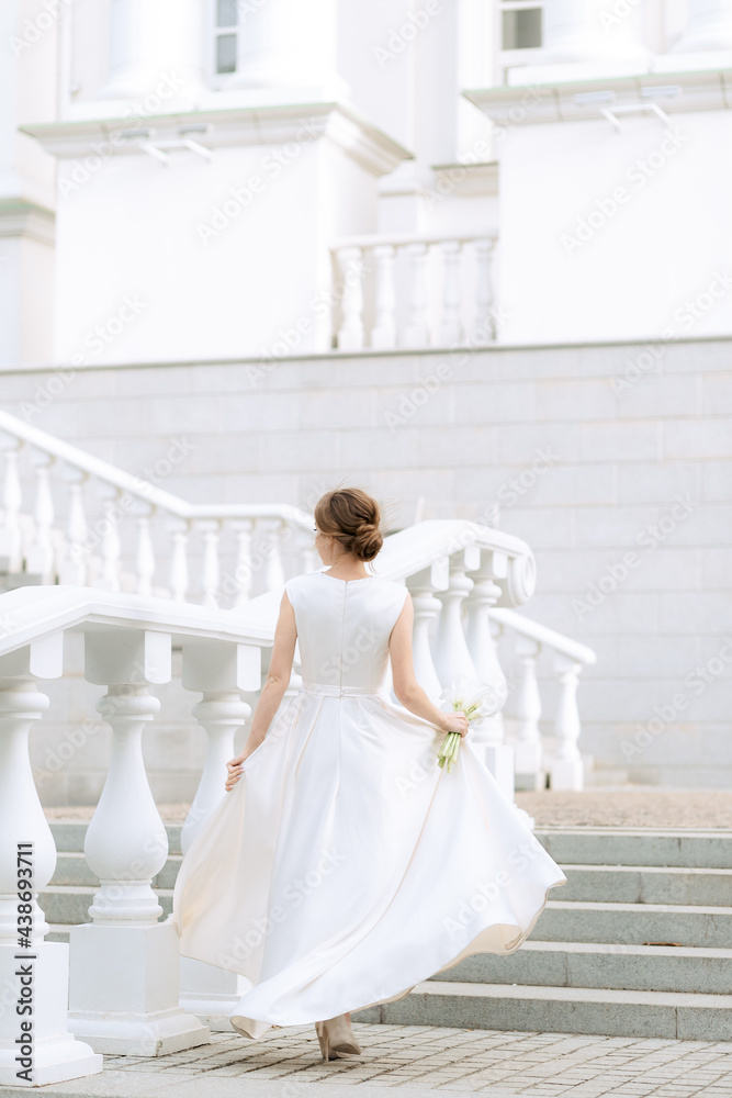 Fototapeta premium portrait of the bride with flowers in a beautiful wedding dress in full growth climbing the stairs, a young blonde, gentle photo wedding portrait