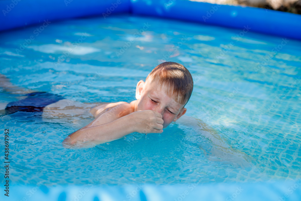 blonde boy in blue swimming trunks swims in an inflatable pool