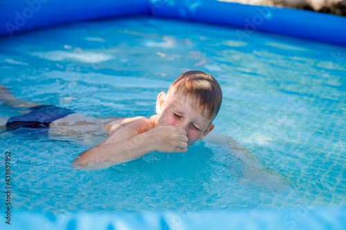 blonde boy in blue swimming trunks swims in an inflatable pool